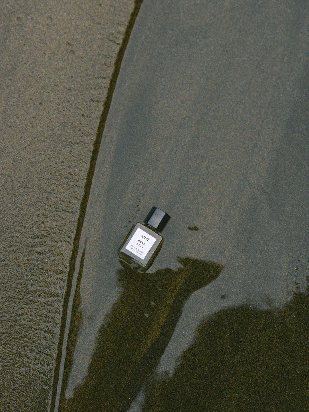 A bottle of Cyan Nori Parfum Extrait – for joy, made by Abel with therapeutic-grade essential oils, sitting in the sand.