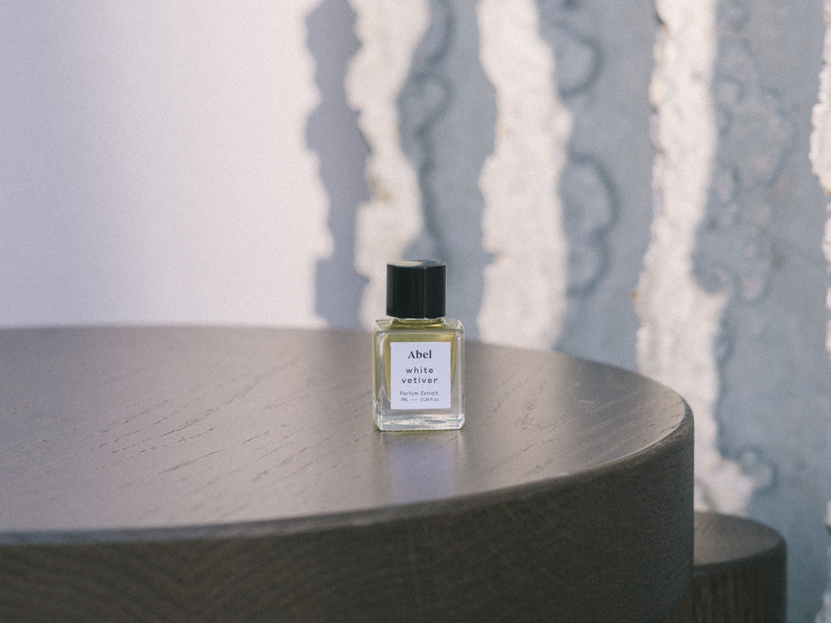 A small bottle of Abel&#39;s White Vetiver Parfum Extrait – for energy, in a 100% Natural Parfum Extrait formulation, delicately placed on a wooden table.