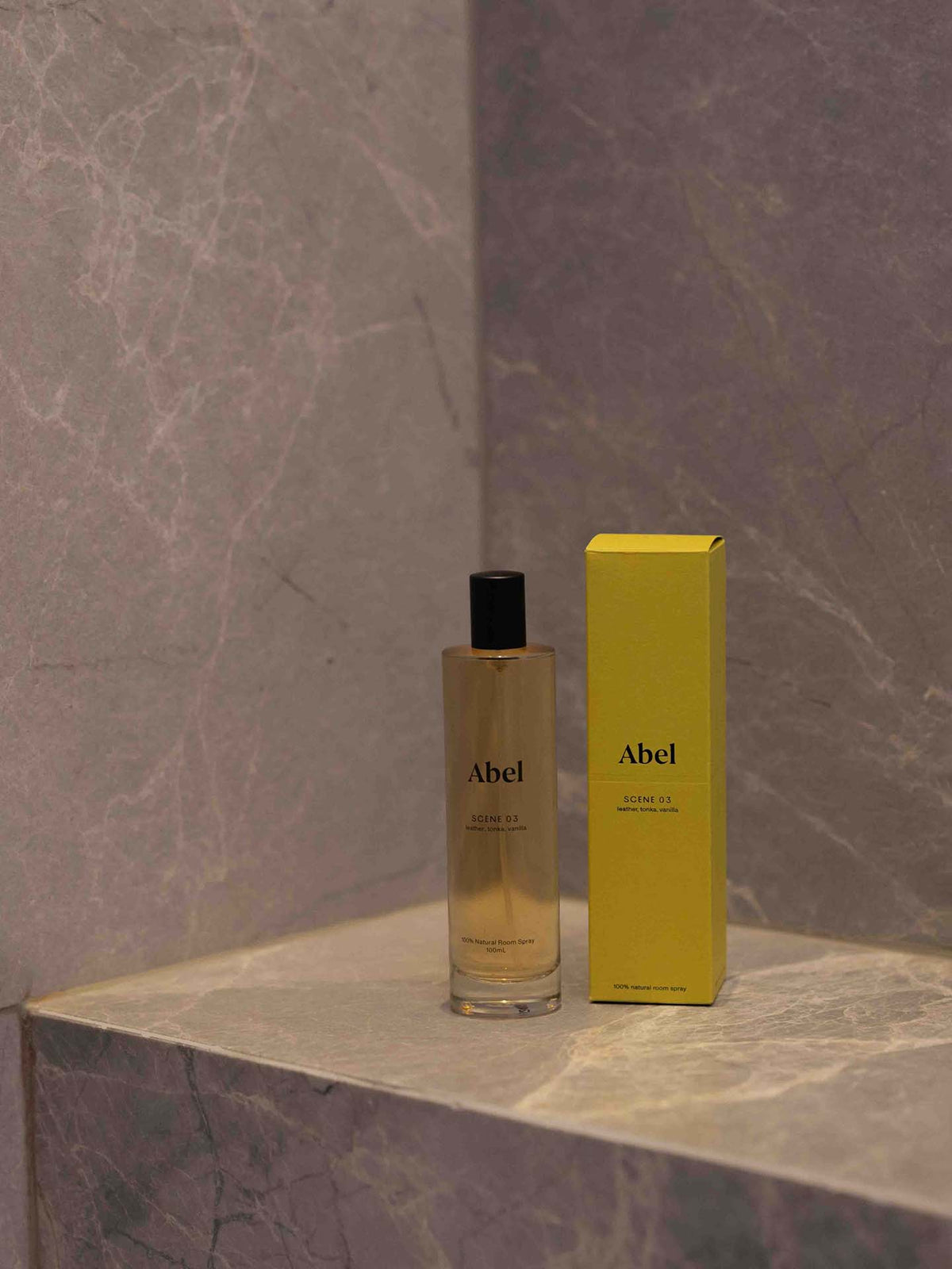 A bottle of Abel Room Spray – Scene 03, featuring notes of leather, tonka, and vanilla, rests with its yellow box on a marbled surface.