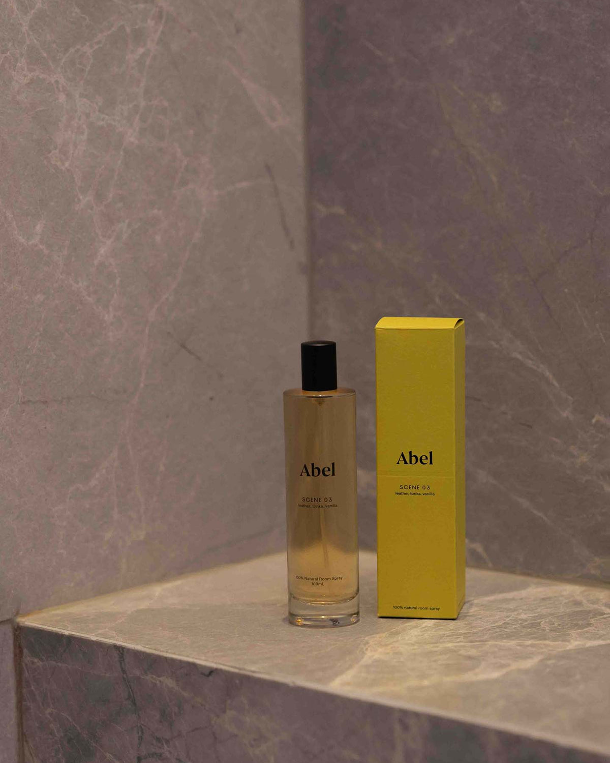 A bottle of Abel Room Spray – Scene 03, featuring notes of leather, tonka, and vanilla, rests with its yellow box on a marbled surface.