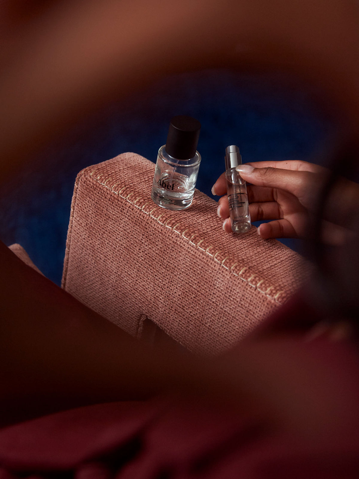 A person holds Abel&#39;s The Apartment Mini spray bottle next to a larger one on a pink textured surface, exuding an air of Parisian chic reminiscent of its dark and sophisticated gourmand scent.