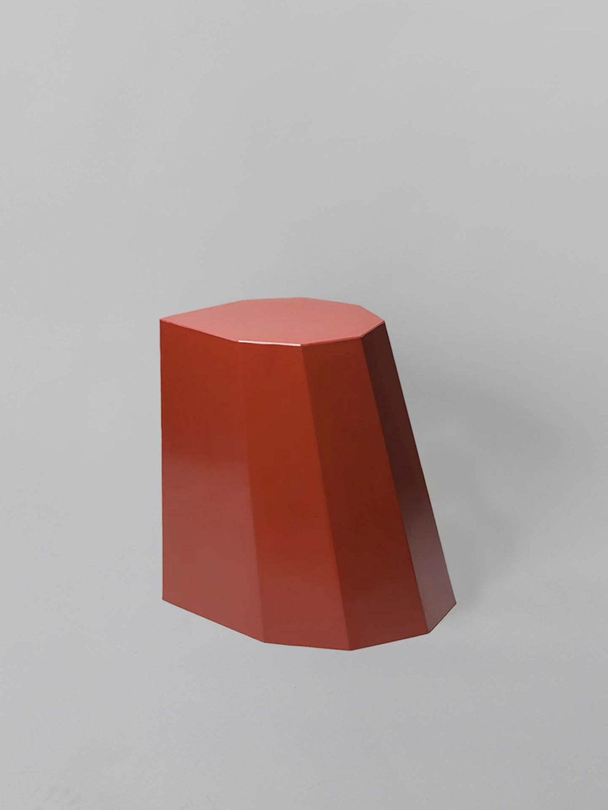 The Heritage Red Arnold Circus Stool, designed by Martino Gamper, boasts angular sides and a flat top reminiscent of geometric shapes. Made from recyclable polyethylene plastic, it is elegantly showcased against a gray background.