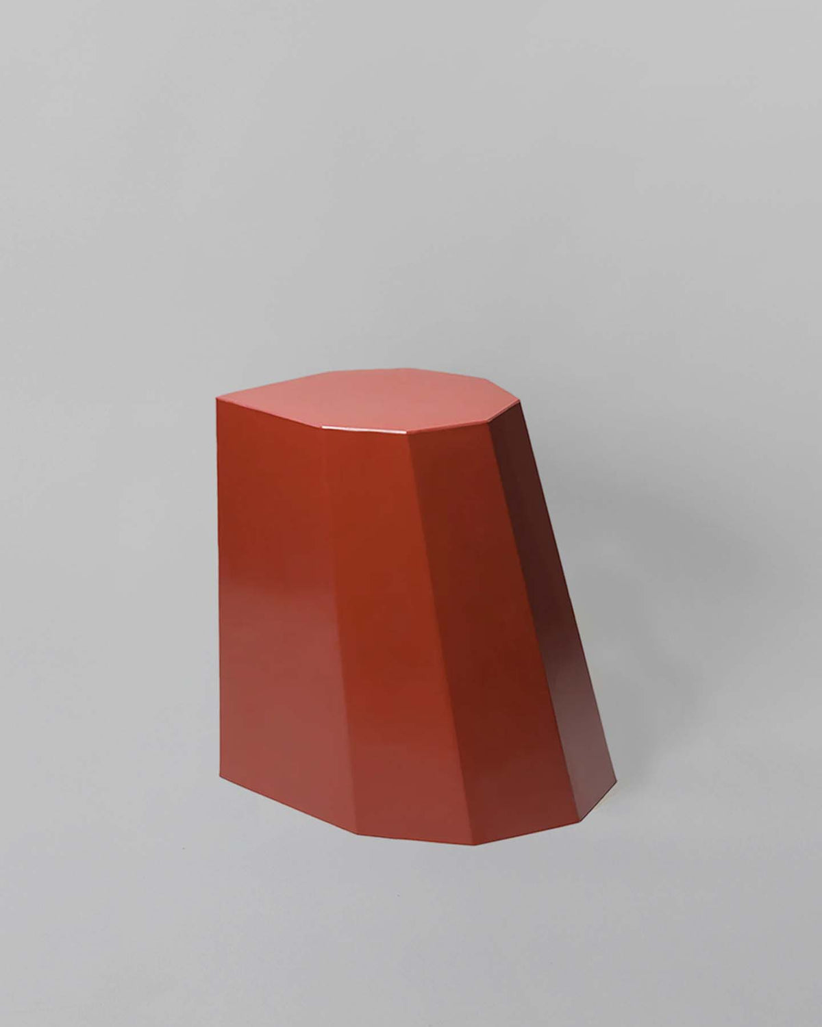 The Heritage Red Arnold Circus Stool, designed by Martino Gamper, boasts angular sides and a flat top reminiscent of geometric shapes. Made from recyclable polyethylene plastic, it is elegantly showcased against a gray background.