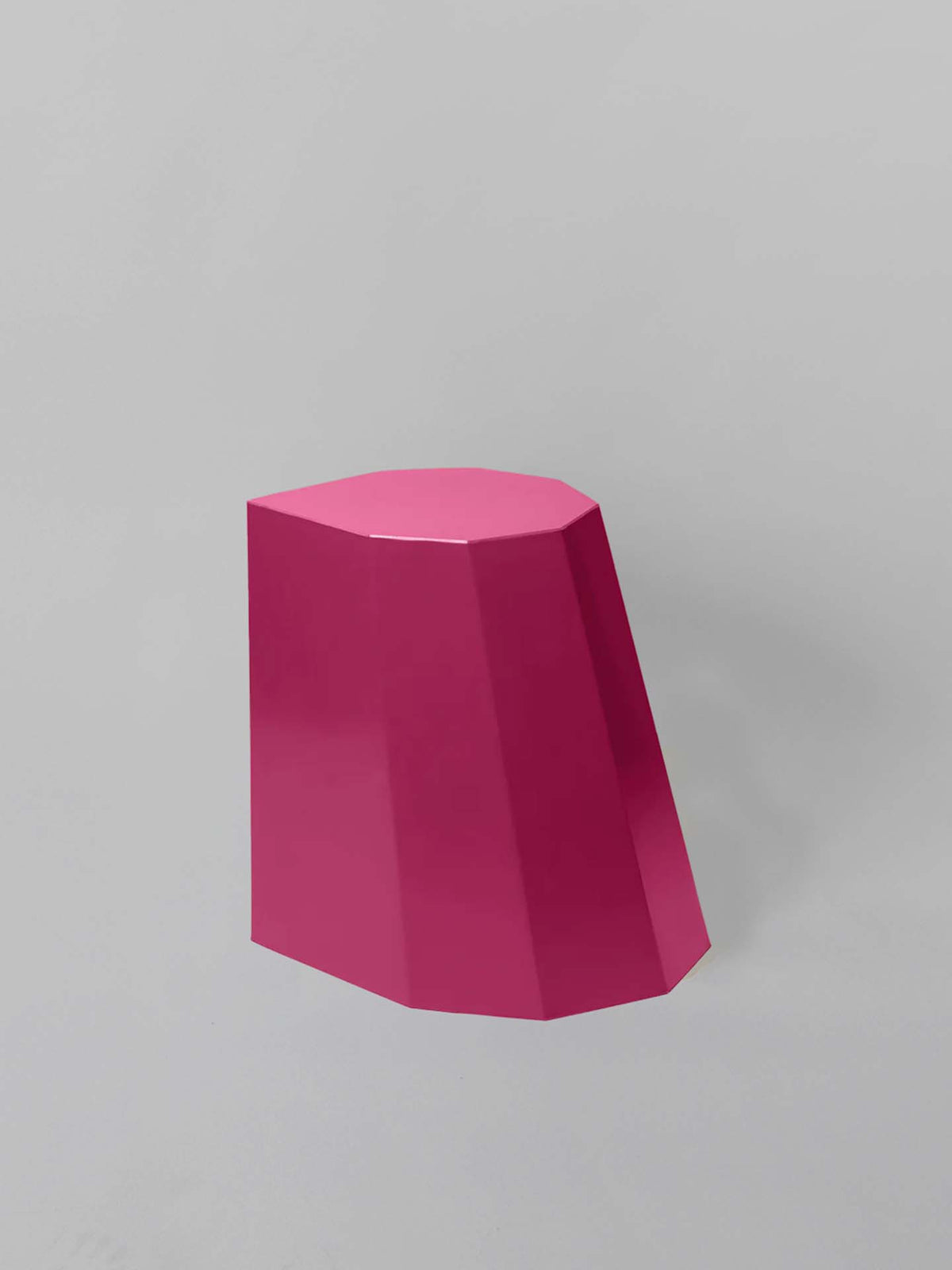 The Arnold Circus Stool – Magenta by Martino Gamper, crafted from recyclable polyethylene with a geometric and angular design, stands with its flat top against a muted gray background.