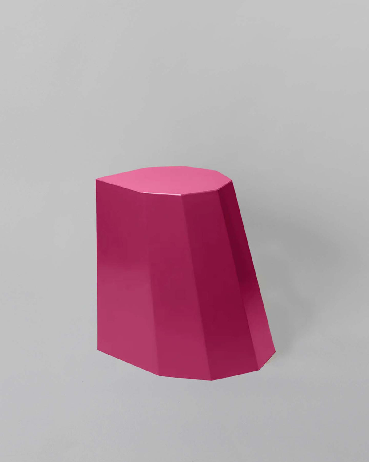 The Arnold Circus Stool – Magenta by Martino Gamper, crafted from recyclable polyethylene with a geometric and angular design, stands with its flat top against a muted gray background.