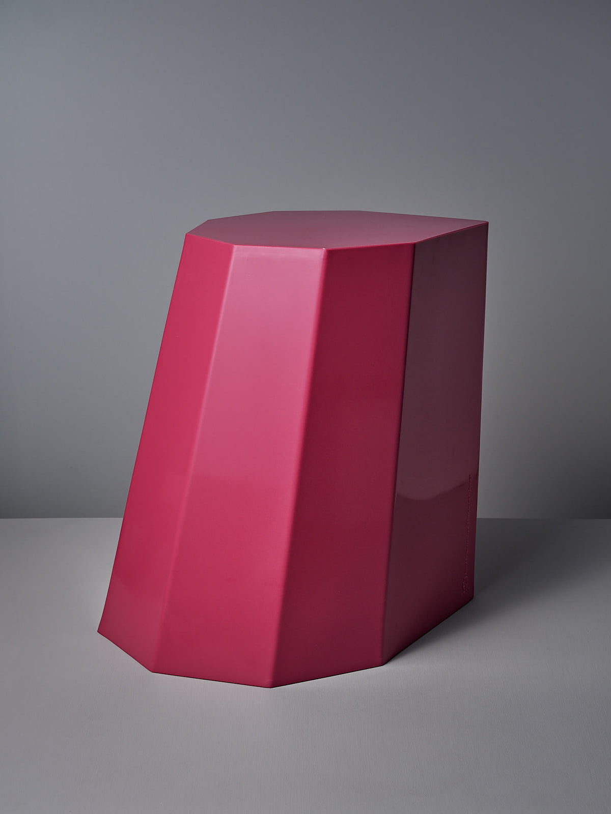 The Arnold Circus Stool in Magenta by Martino Gamper is a large, geometric sculpture crafted from recyclable polyethylene. Its angular, faceted design features smooth surfaces and is displayed against a gray backdrop.