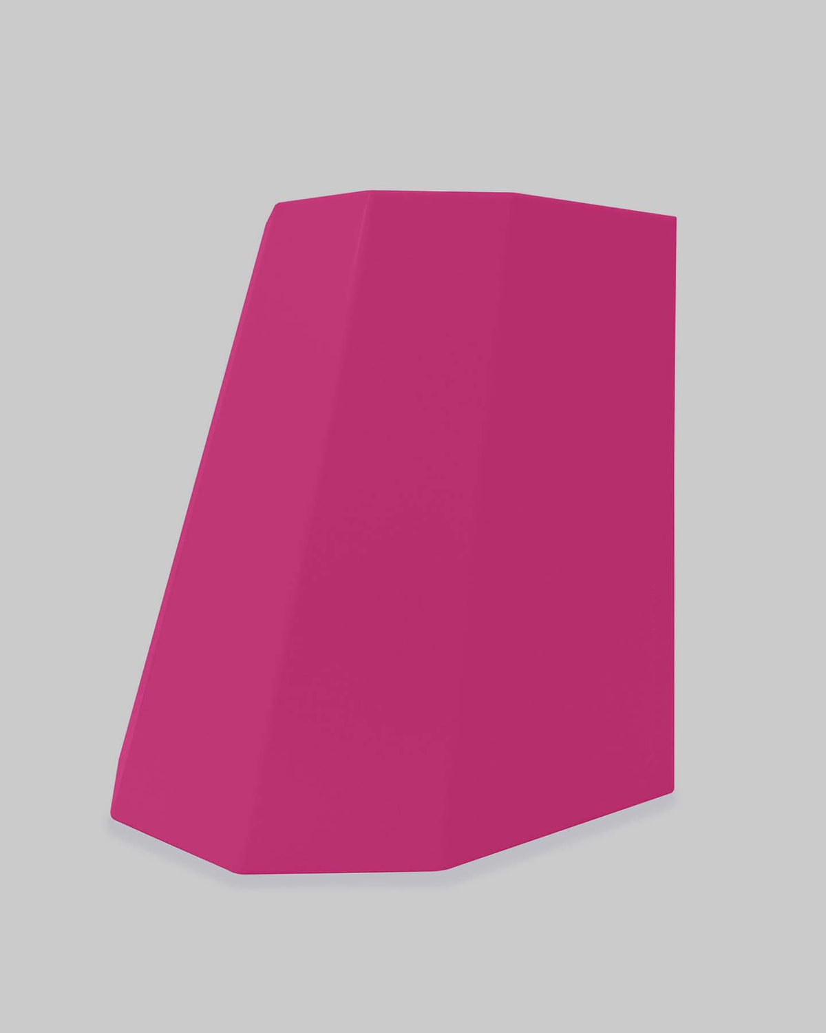 A magenta geometric object, the Arnold Circus Stool by Martino Gamper, with a slanted rectangular shape crafted from recyclable polyethylene, stands against a light gray background.