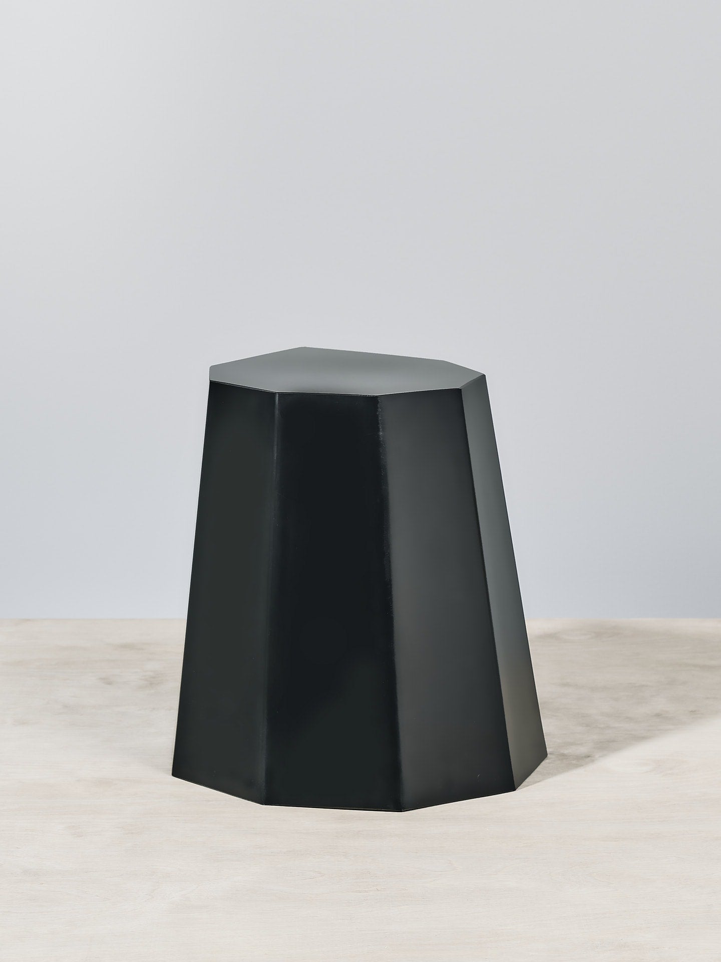A Arnoldino Stool – Black by Martino Gamper on top of a wooden table.