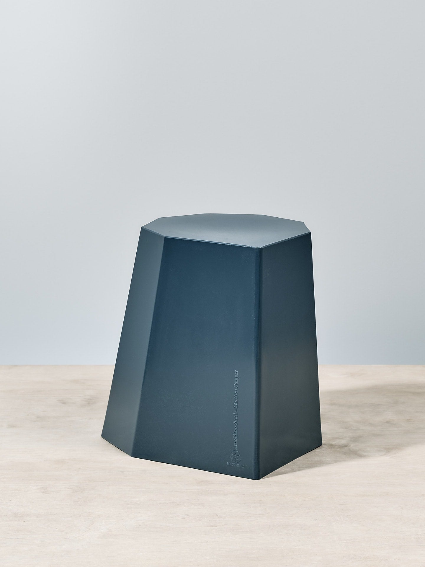 An Arnoldino Stool – Navy sitting on top of a wooden table, Martino Gamper.