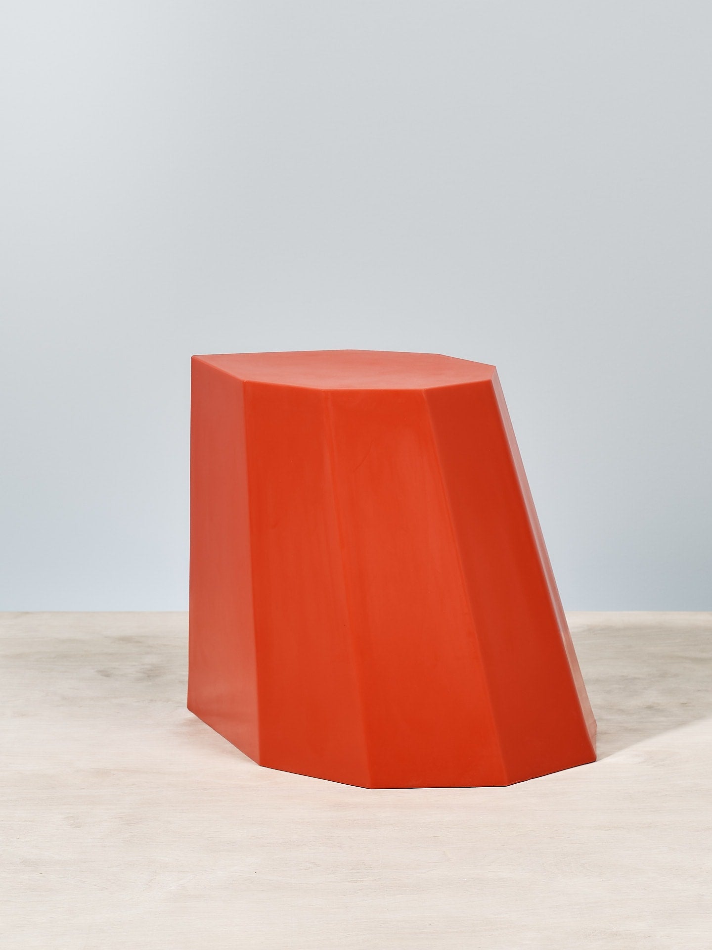 An Arnoldino Stool – Red by Martino Gamper sitting on top of a wooden table.