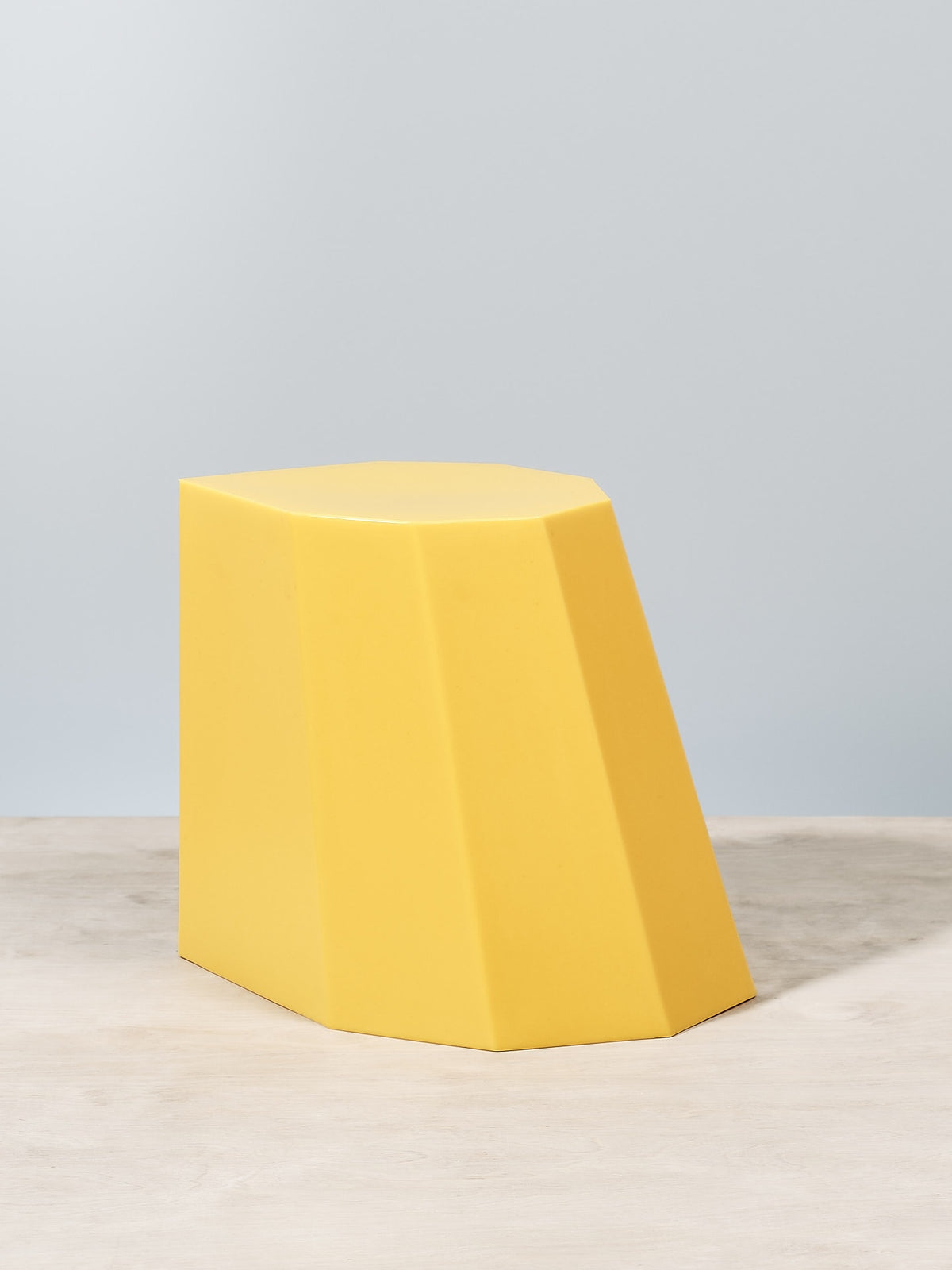 An Arnoldino Stool – Yellow sitting on top of a wooden table by Martino Gamper.