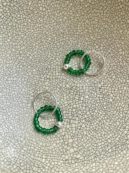 Two Kākāriki Sleepers hoop earrings on a plate by Avara Studio.