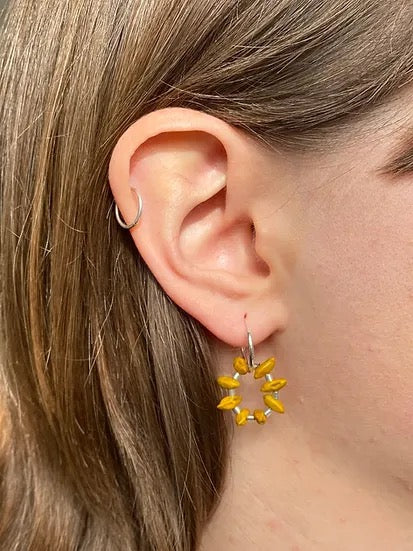 A woman&#39;s ear with a pair of Kōwhai Circle Sleepers earrings from Avara Studio.