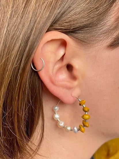 A woman&#39;s ear with a Kōwhai + Pearl Hoops earring by Avara Studio.