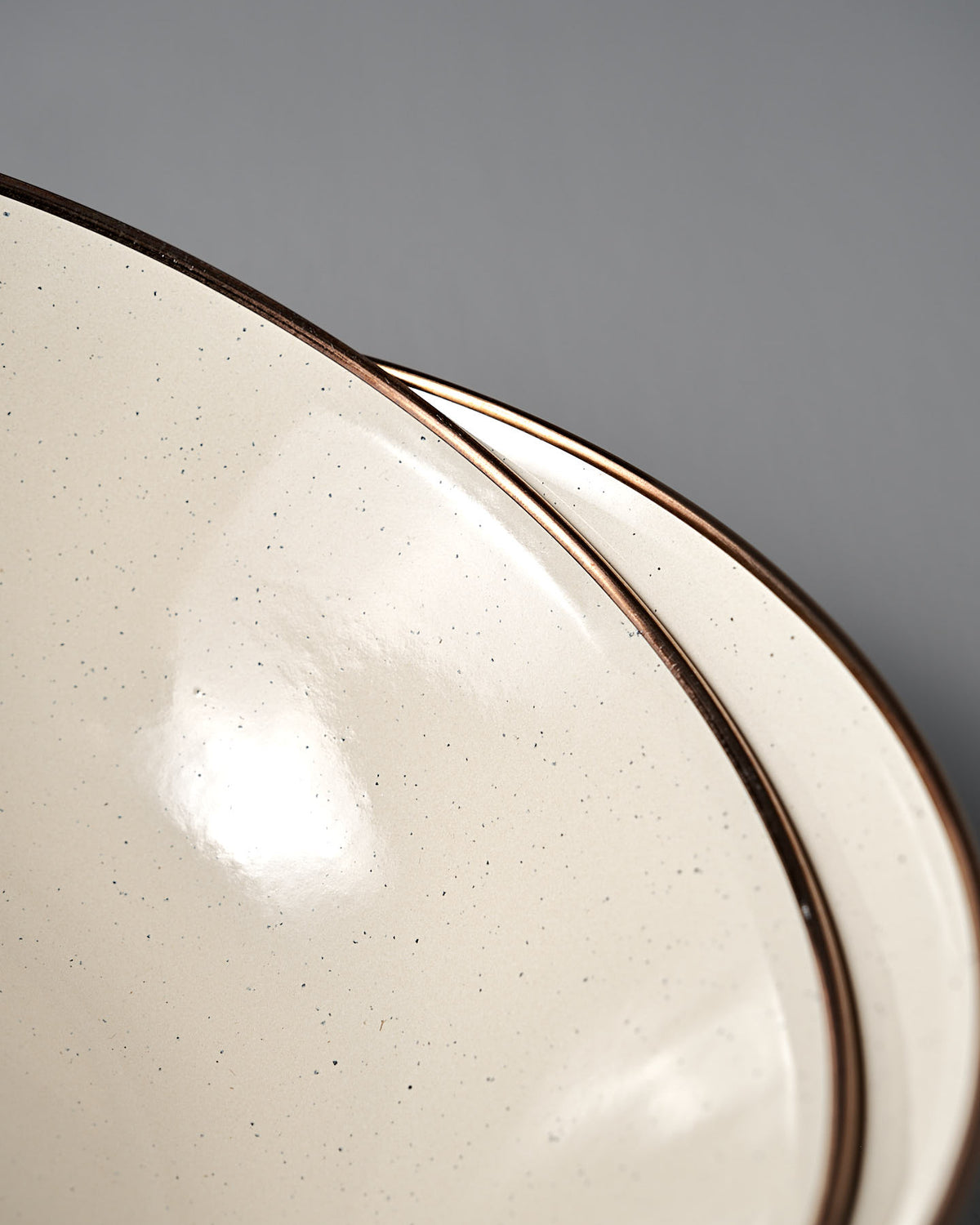 Close-up of two stacked Barebones Enamel Two-Tone Bowls in Olive Drab, featuring a vintage-inspired design with cream and brown edges, set against a gray background. Set of 2.