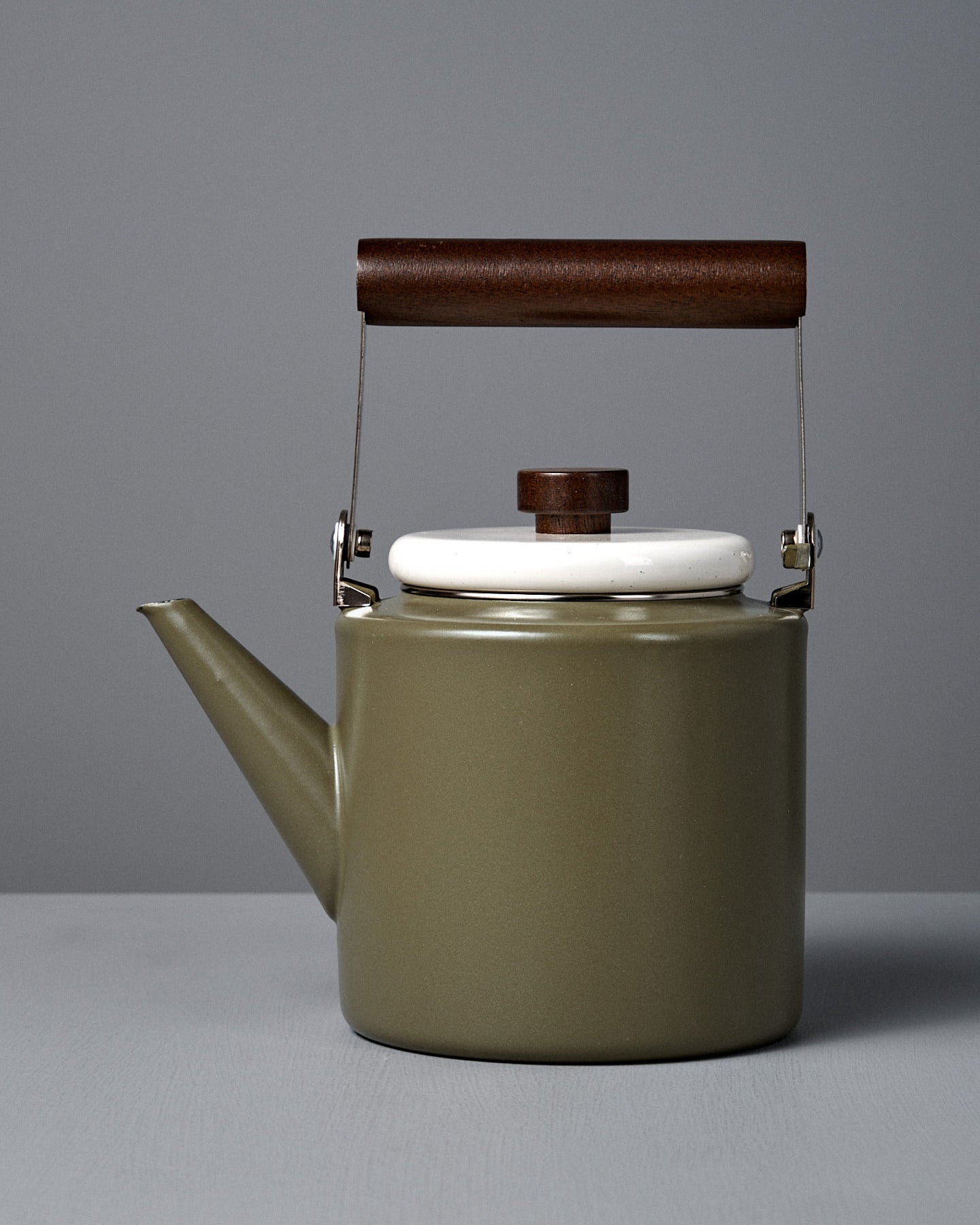 The Enamel Two-Tone Kettle – Olive Drab features a green finish, white lid, and dark walnut handle, displayed on a plain gray background.