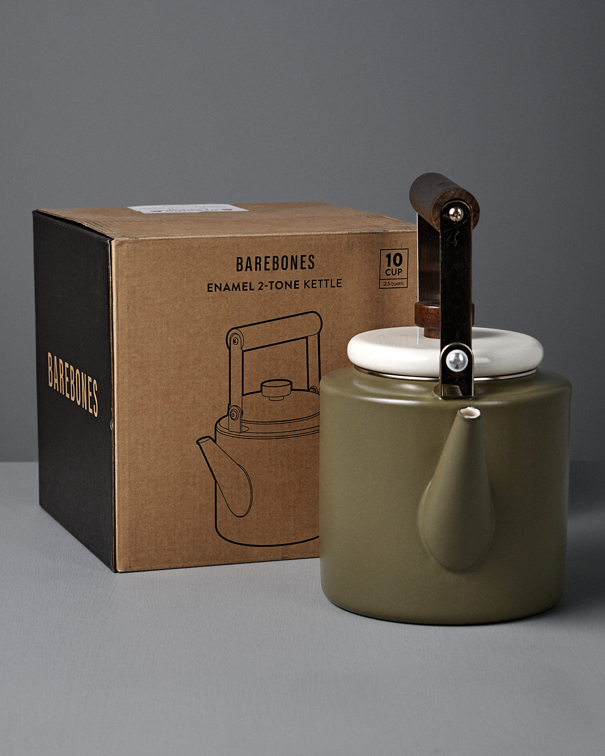 A vintage-style enamelware kettle with a walnut handle rests next to its box labeled "Enamel Two-Tone Kettle – Olive Drab.