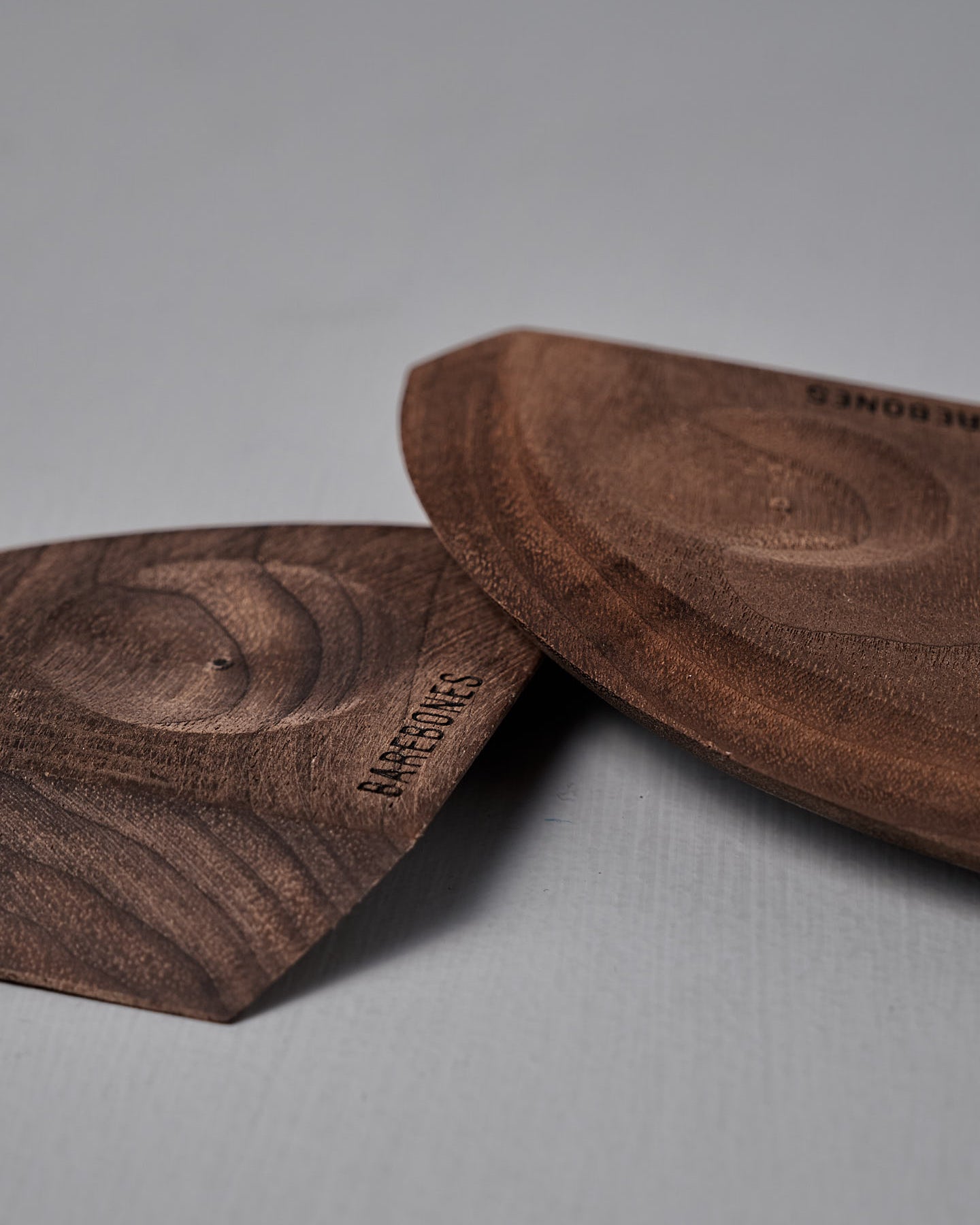 The Barebones Cast Iron Wood Scraper, an ergonomic tool for cleaning cookware, features a branded tag attached by a black string and is shown on a gray surface.