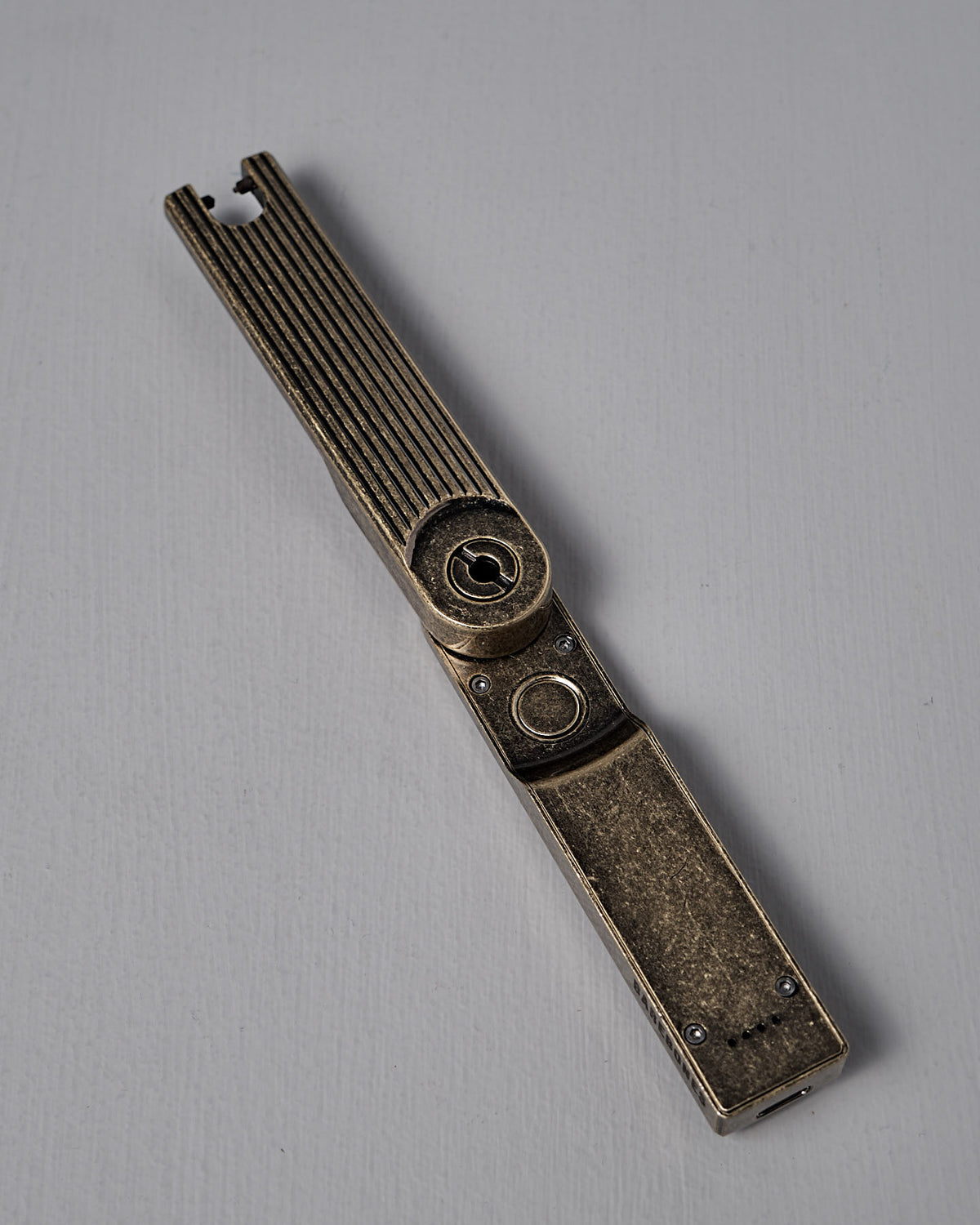 The Barebones Pivot Arc Lighter features a vintage metal design with a rectangular body and long, ridged arm, captured on a plain light surface.
