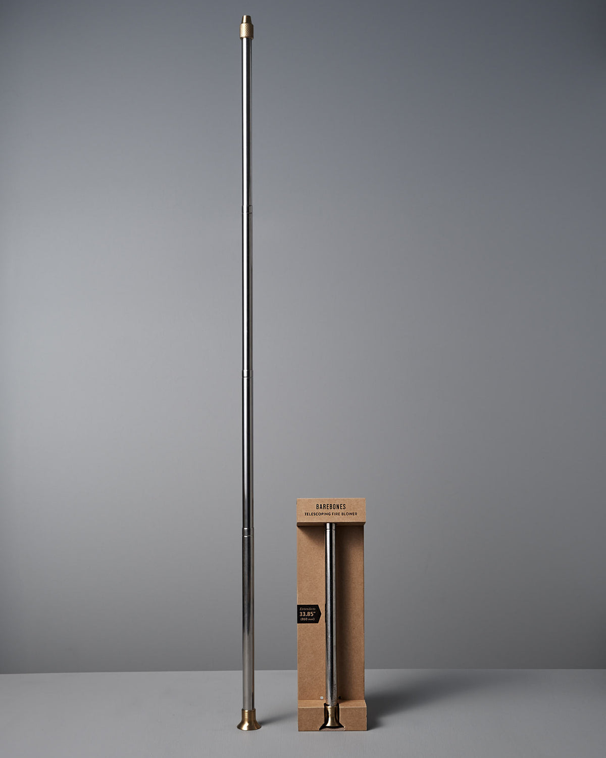 A long, silver Barebones Telescoping Fire Blower with gold-colored tips stands upright beside a shorter, boxed version labeled "Barber’s Pole.