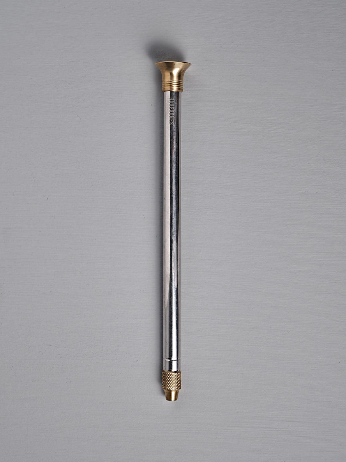 The Barebones Telescoping Fire Blower, with a gold-colored cap and threaded connector, is displayed on a gray background.