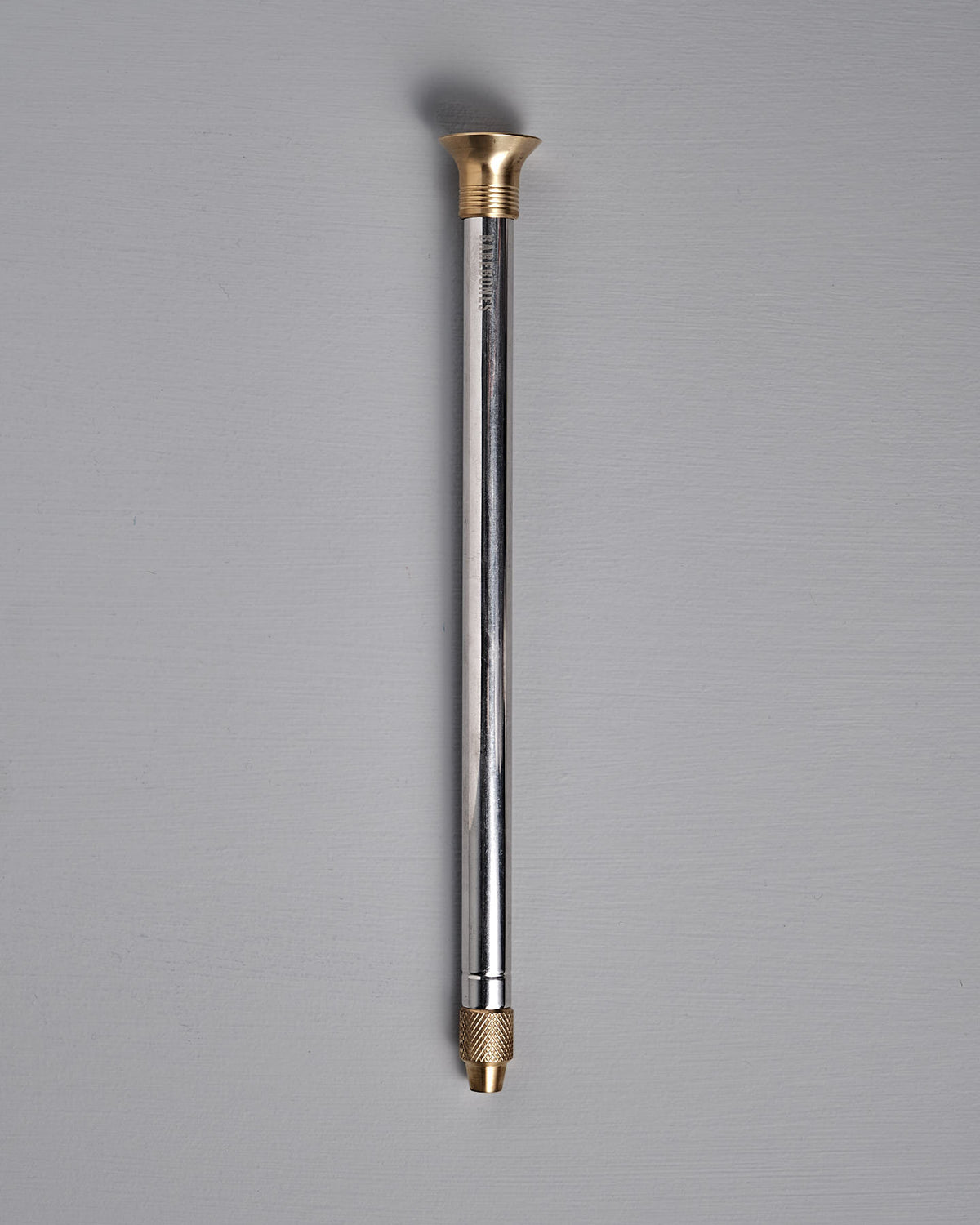 The Barebones Telescoping Fire Blower, with a gold-colored cap and threaded connector, is displayed on a gray background.