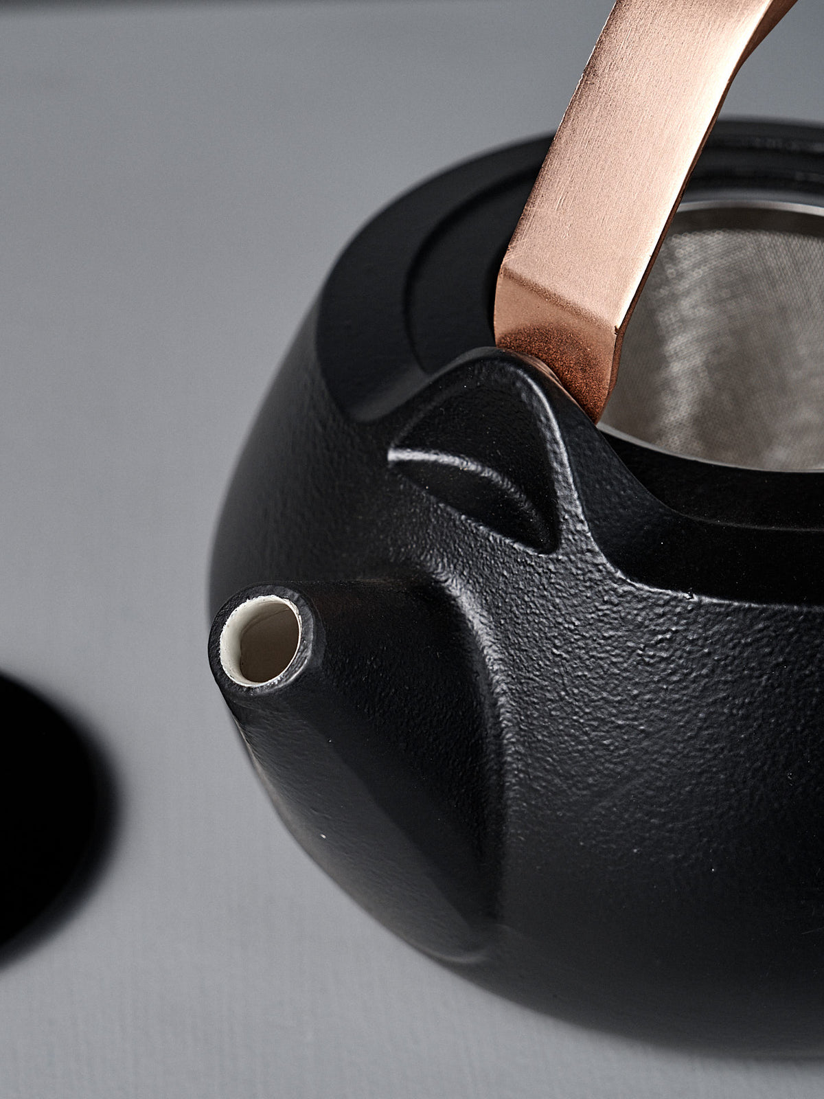 Close-up of the Cast Iron Teapot (Enamel Lined) featuring a copper handle, stainless steel infuser, spout, and lid, placed on a light surface.