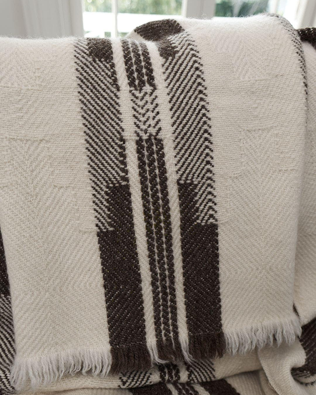 A close-up of a Rodopska Takan Bulgarian Shevitza Wool Blanket – Cream, made from locally sourced wool, draped over a chair, with a window partially visible in the background.