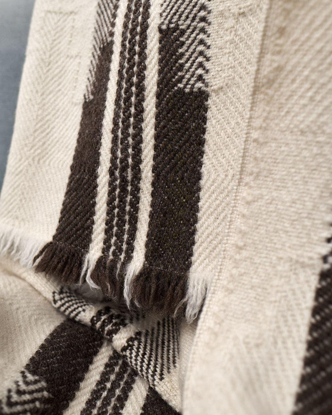 Close-up of a beige and brown striped woven blanket with fringe edges draped over a surface, crafted from locally sourced wool. This is the Bulgarian Shevitza Wool Blanket – Cream by Rodopska Takan.
