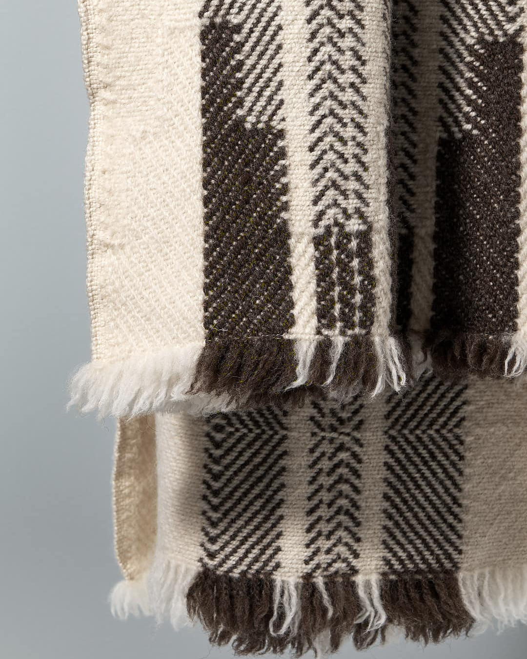 Close-up of a Rodopska Takan Bulgarian Shevitza Wool Blanket – Cream made from locally sourced wool with beige and dark brown stripes and herringbone patterns, hanging against a plain gray background.