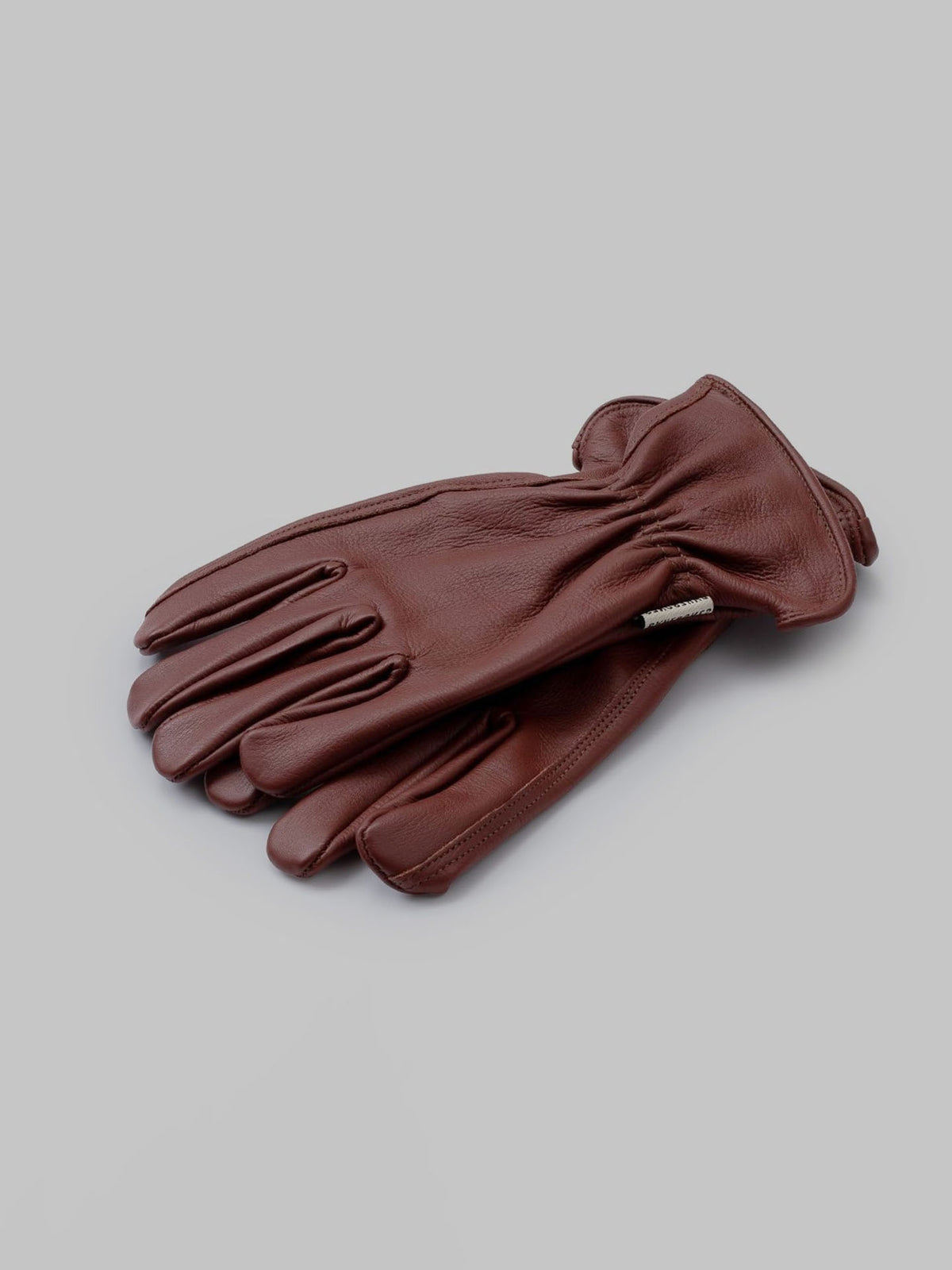 The Classic Work Glove – Cognac by Barebones, crafted from premium grain cowhide, rests elegantly on a gray surface.