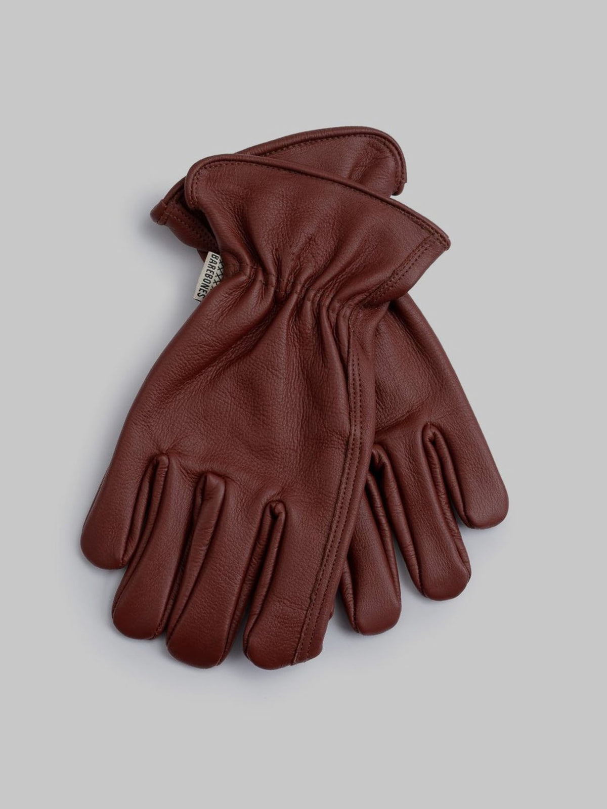 The Classic Work Glove – Cognac by Barebones, made from premium grain cowhide leather, lies on a gray background, exemplifying outdoor versatility and durability.