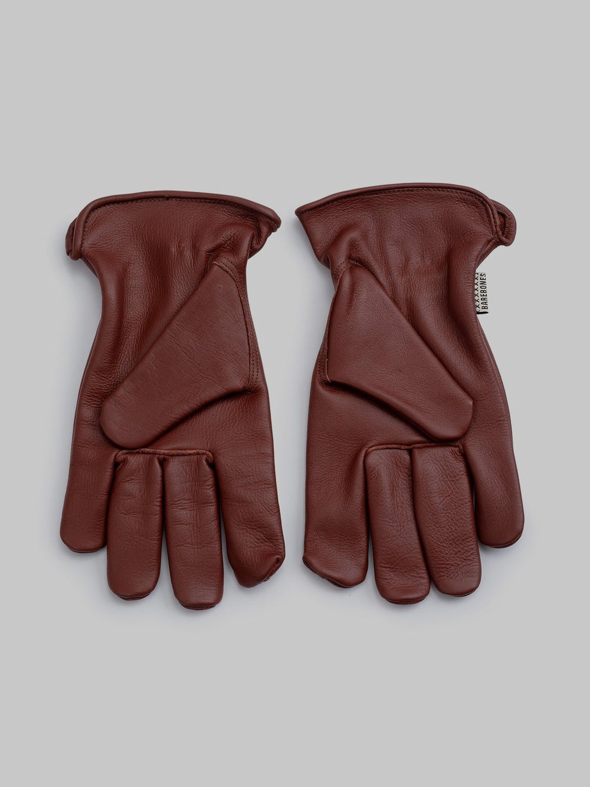 The Classic Work Glove – Cognac by Barebones, crafted from premium grain cowhide, features a unique design with extra padding on the back and an open-ended thumb for outdoor versatility. Displayed against a light gray background.