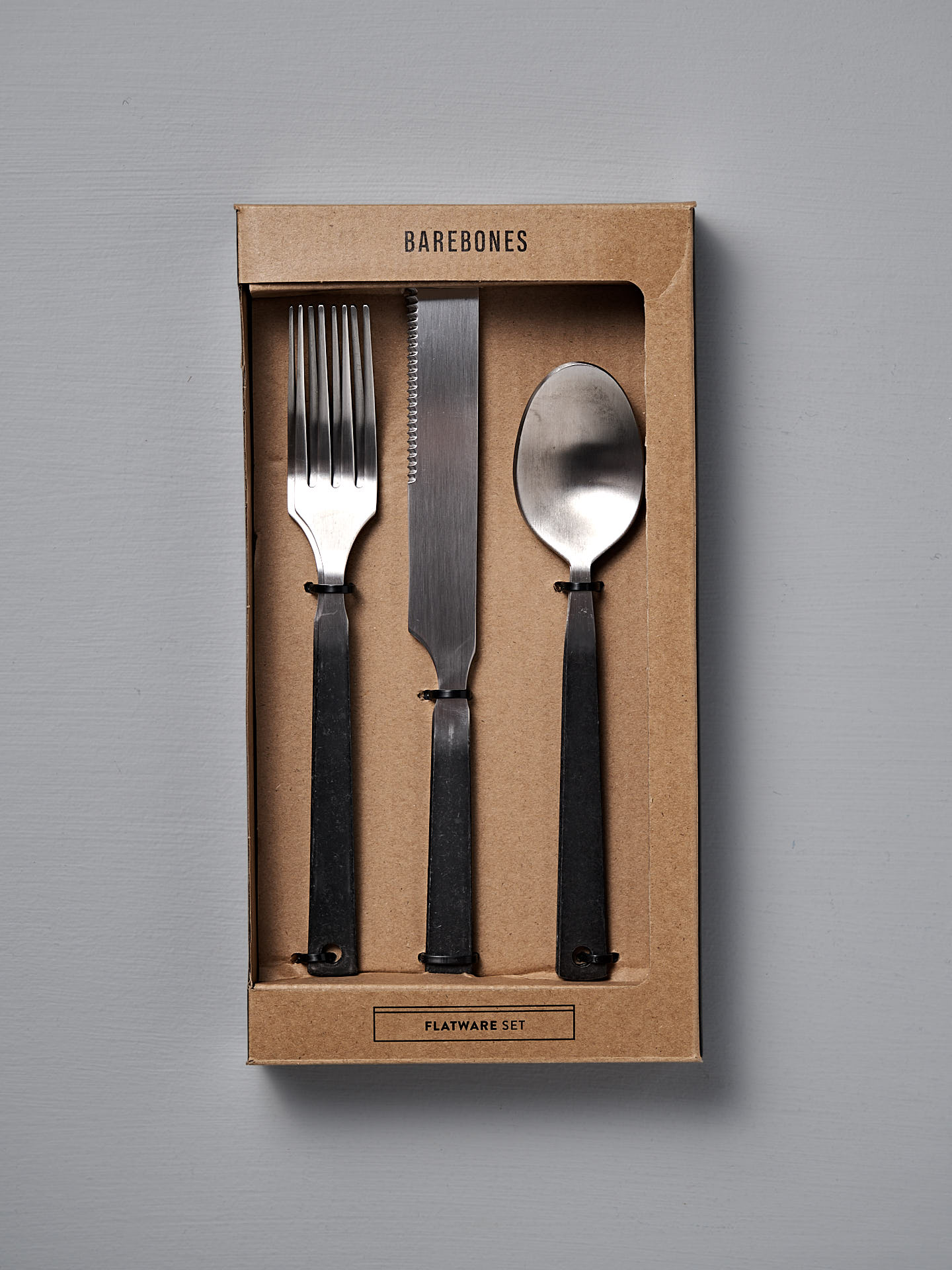 The Barebones Flatware Cutlery Set includes 2 forks, knives, and spoons with black handles and modern design, crafted from durable stainless steel. Displayed boxed against a gray background.