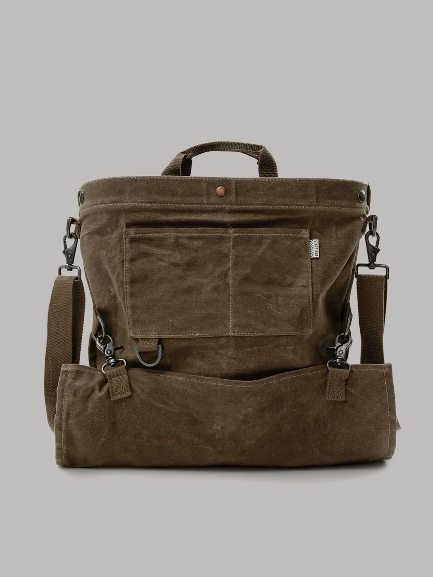 The Gathering Bag – Khaki by Barebones is a khaki paraffin waxed canvas backpack featuring adjustable shoulder straps, a front pocket, and metal hardware. It showcases a vintage orchard design set beautifully against a plain grey background.