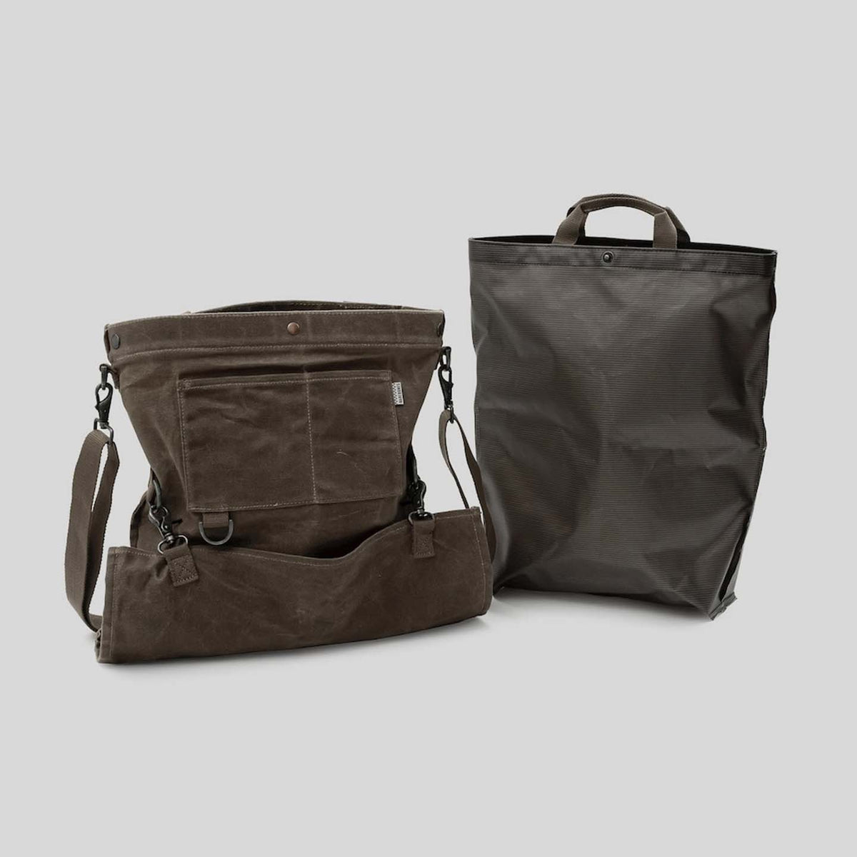 Two canvas bags from Barebones: a khaki Gathering Bag, inspired by vintage design, featuring multiple pockets and an adjustable strap made from paraffin-waxed canvas, along with another closed bag in deep brown hues, equipped with a top handle.