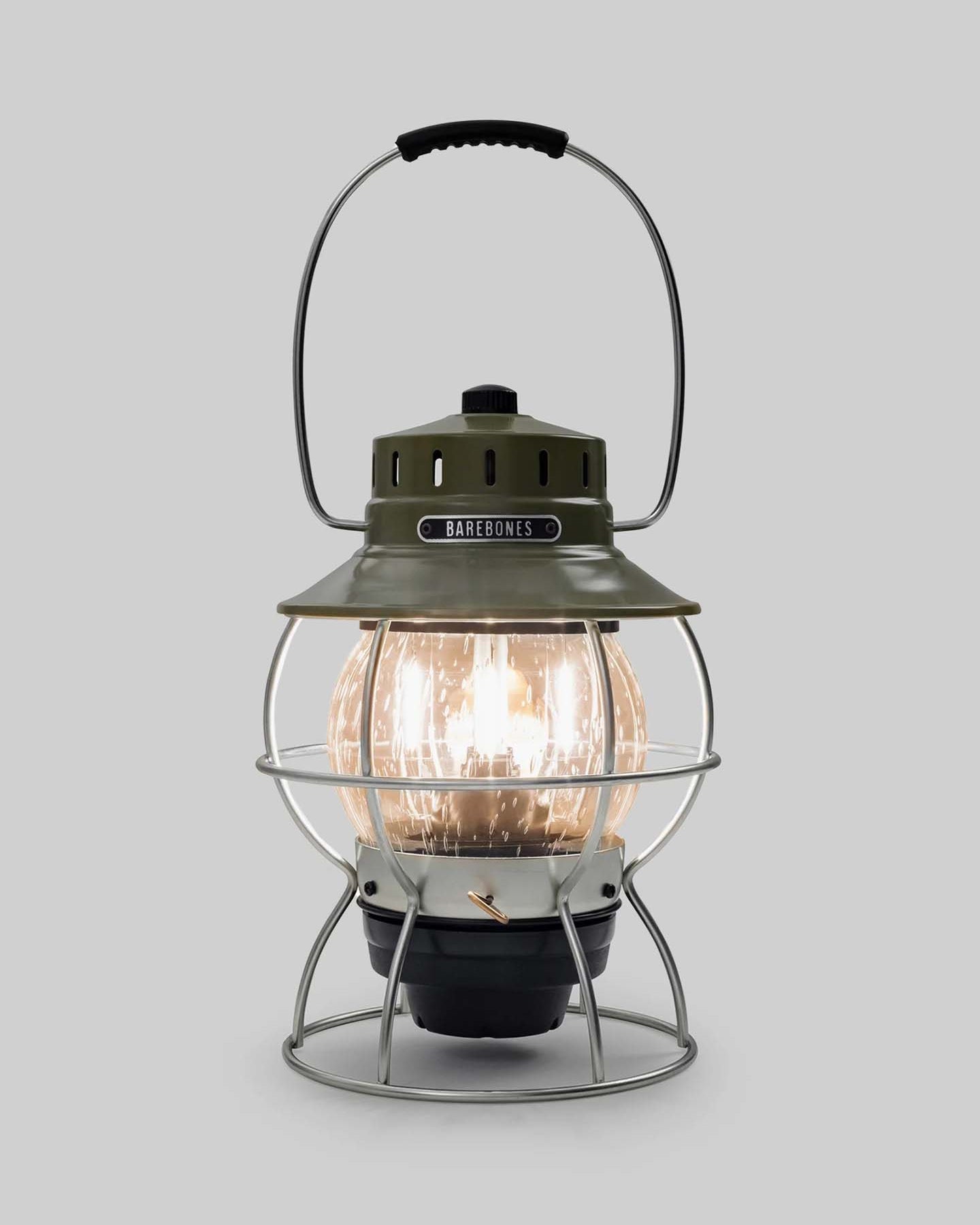 The Railroad Lantern – Olive Drab by Barebones, showcasing an Edison-style LED bulb and a transparent glass globe with a vintage-style olive green top, is set against a plain gray background.