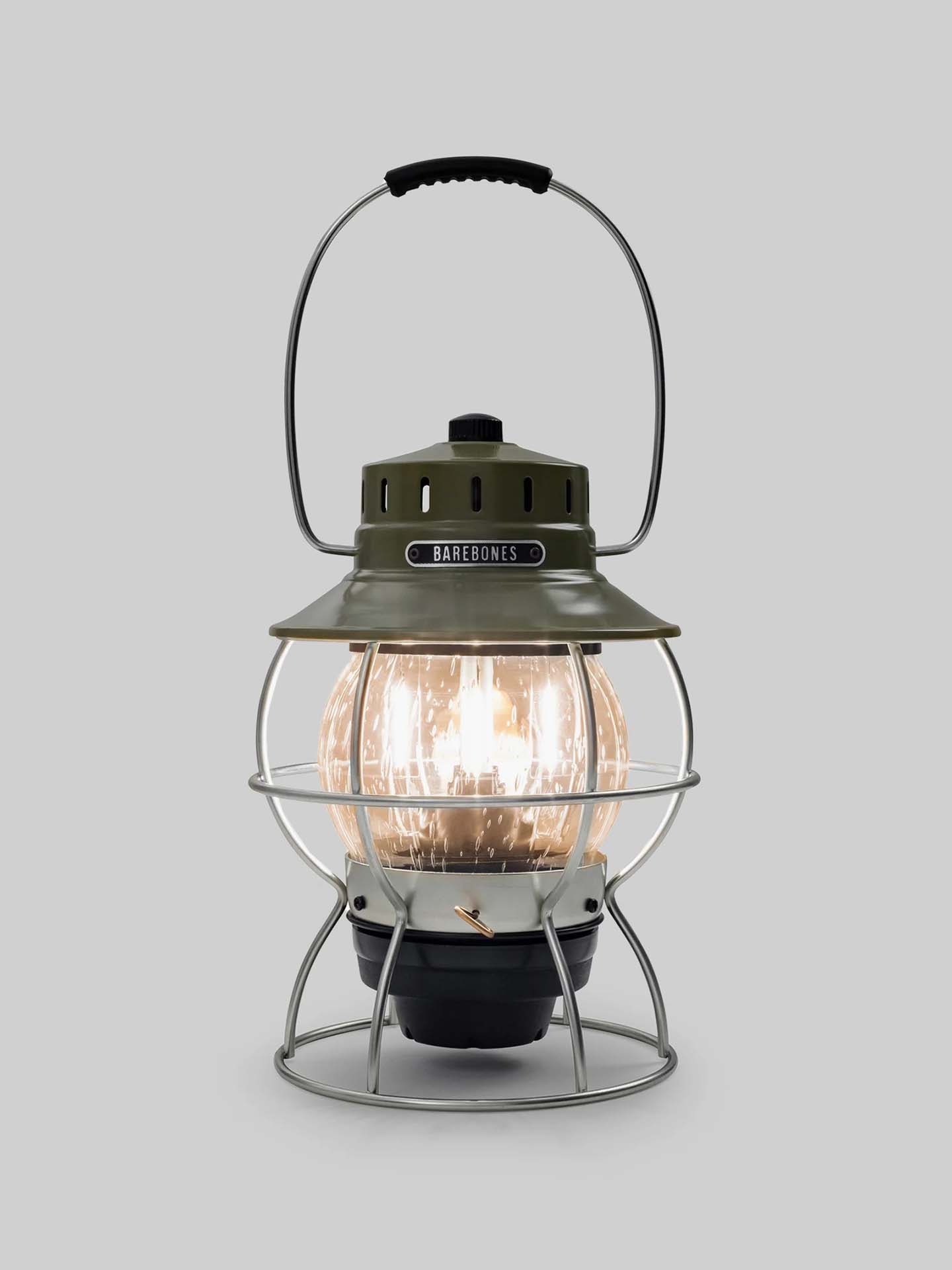 The Railroad Lantern – Olive Drab by Barebones, showcasing an Edison-style LED bulb and a transparent glass globe with a vintage-style olive green top, is set against a plain gray background.