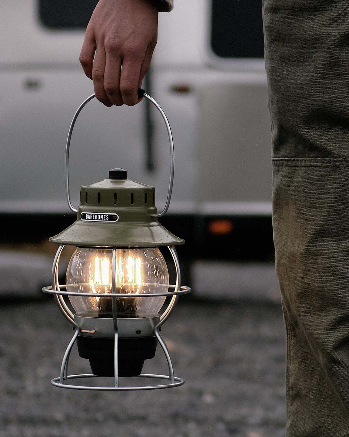 The Railroad Lantern – Olive Drab by Barebones, showcasing an Edison-style LED bulb and a transparent glass globe with a vintage-style olive green top, is set against a plain gray background.