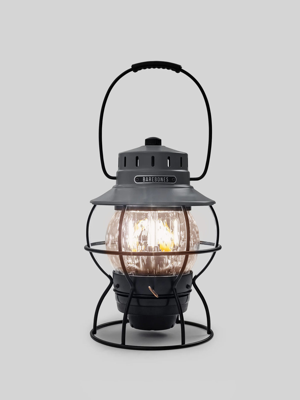 The Barebones Railroad Lantern in Slate Grey is a vintage-style LED light featuring a metal cage, handle, and glowing Edison-style bulb.