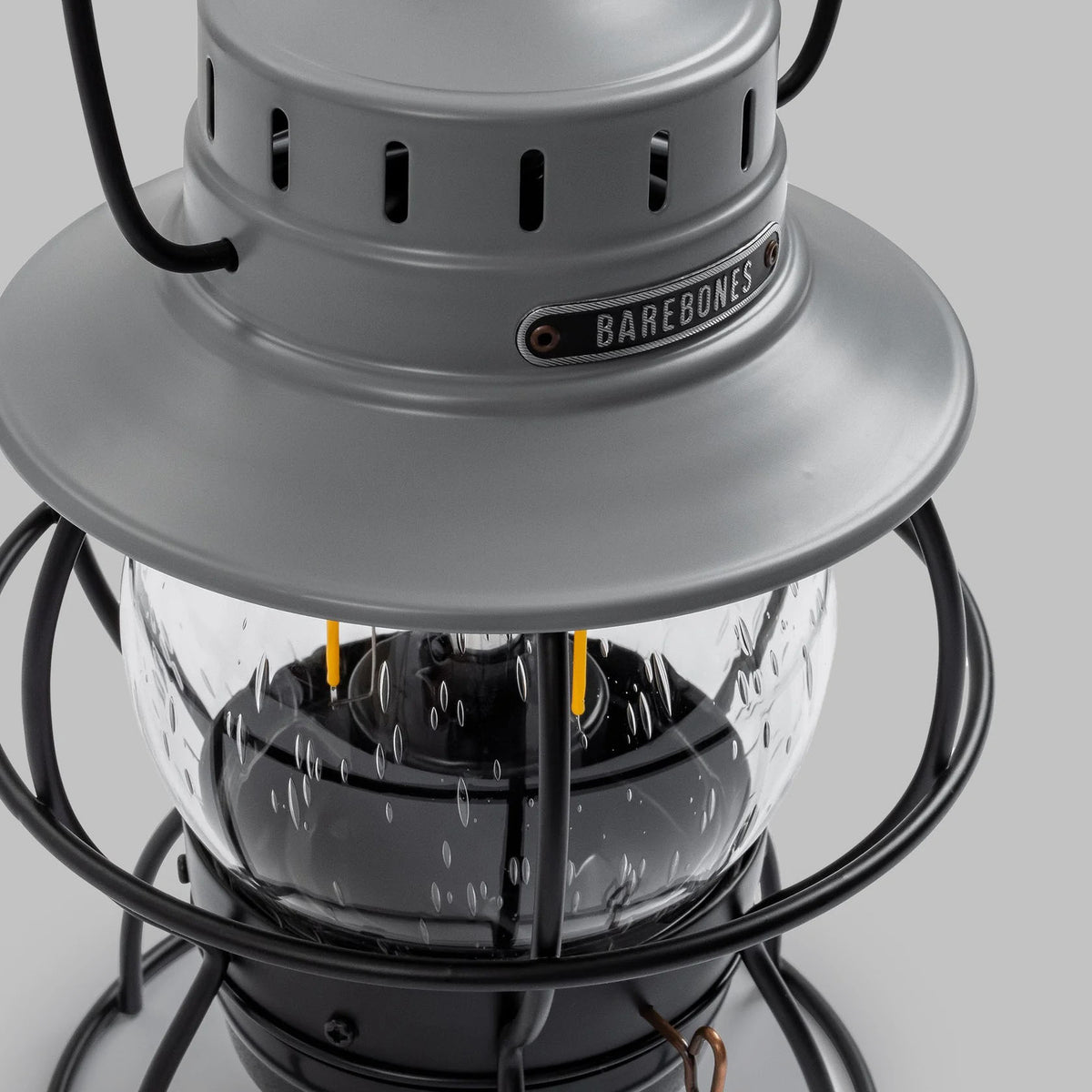 Close-up of the Barebones &quot;Railroad Lantern – Slate Grey&quot; with a glass enclosure and LED filament lights resembling an Edison bulb. This charming lantern features a rechargeable battery for endless illumination possibilities.