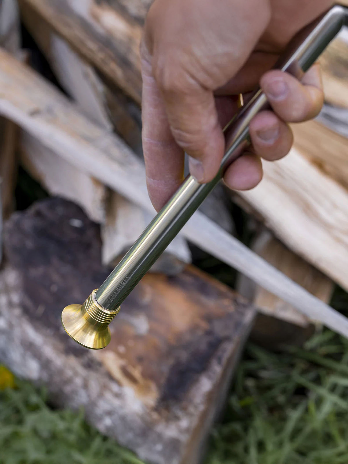 A hand holds a Barebones Telescoping Fire Blower with a flat tip in front of stacked firewood.