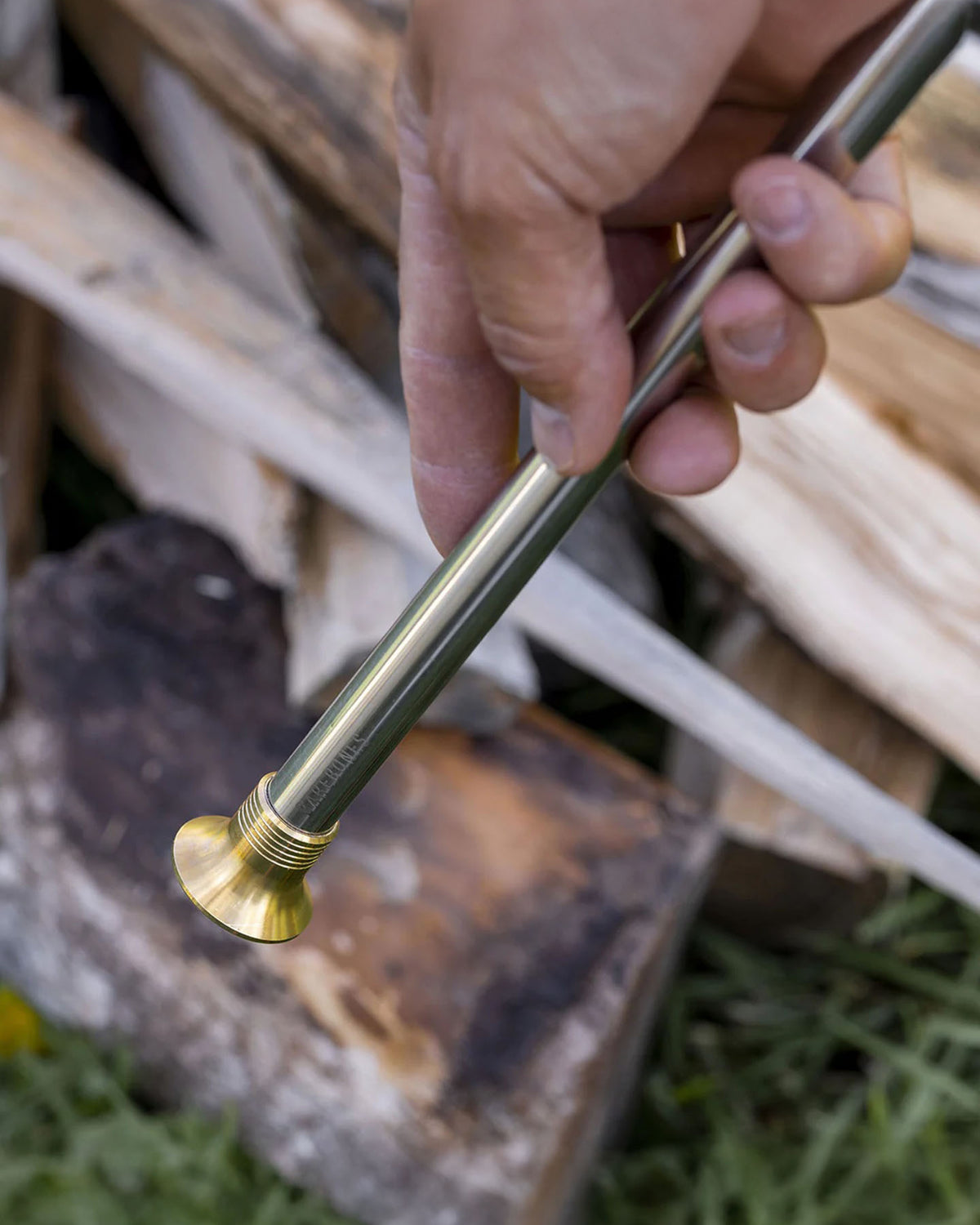A hand holds a Barebones Telescoping Fire Blower with a flat tip in front of stacked firewood.