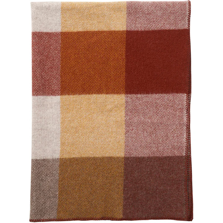 A folded Klippan Block Wool Throw – Rust with a large plaid pattern in colors such as red, beige, brown, yellow, and pink, made from eco-friendly New Zealand lambswool for comfort and sustainability.