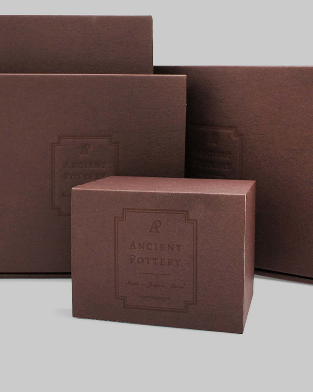 Three boxes of varying sizes, each with a brown finish and labeled "Ancient Pottery," are set against a light gray backdrop, evoking the elegance of Japanese craftsmanship. These boxes could contain treasures such as a Mino-yaki Coffee Dripper by CHIPS Inc. or other handmade stoneware gems.