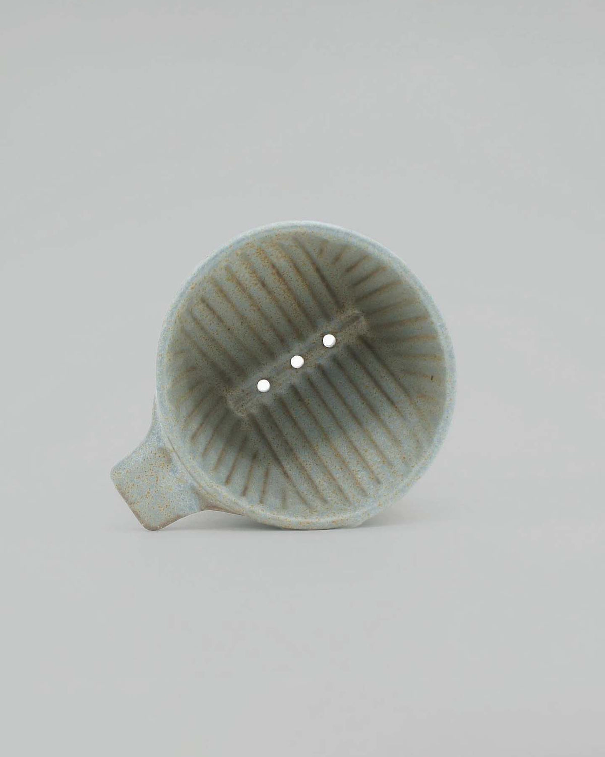 Perched against a plain backdrop, the Mino-yaki Coffee Dripper (2 Cup) – Grey by CHIPS Inc. showcases the exquisite craftsmanship of traditional Mino-yaki ceramics. Made in Japan and harking back to ancient pottery, this light gray dripper features three precisely aligned holes for optimal brewing.