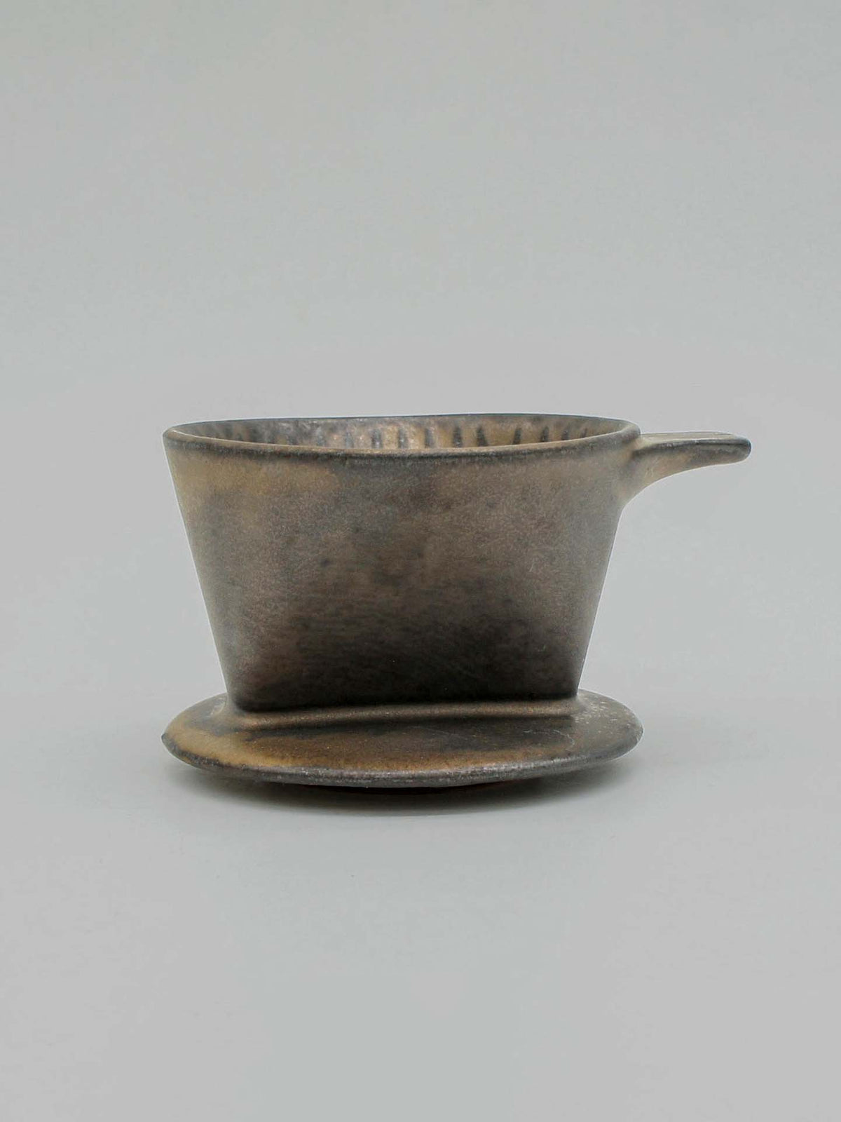 A brass-toned Mino-yaki Coffee Dripper (2 Cup) by CHIPS Inc. with a handle sits elegantly on a matching saucer against a plain background, fusing modern aesthetics with ancient pottery traditions.