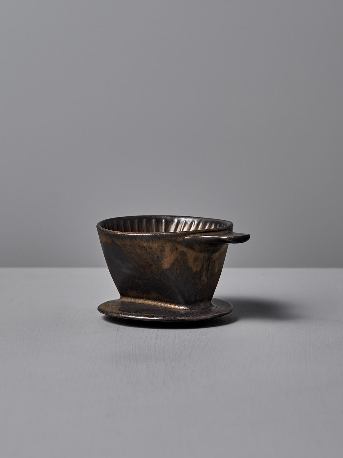 The CHIPS Inc. Mino-yaki Coffee Dripper (2 Cup) in brass elegantly sits on a smooth gray surface against a matching backdrop.