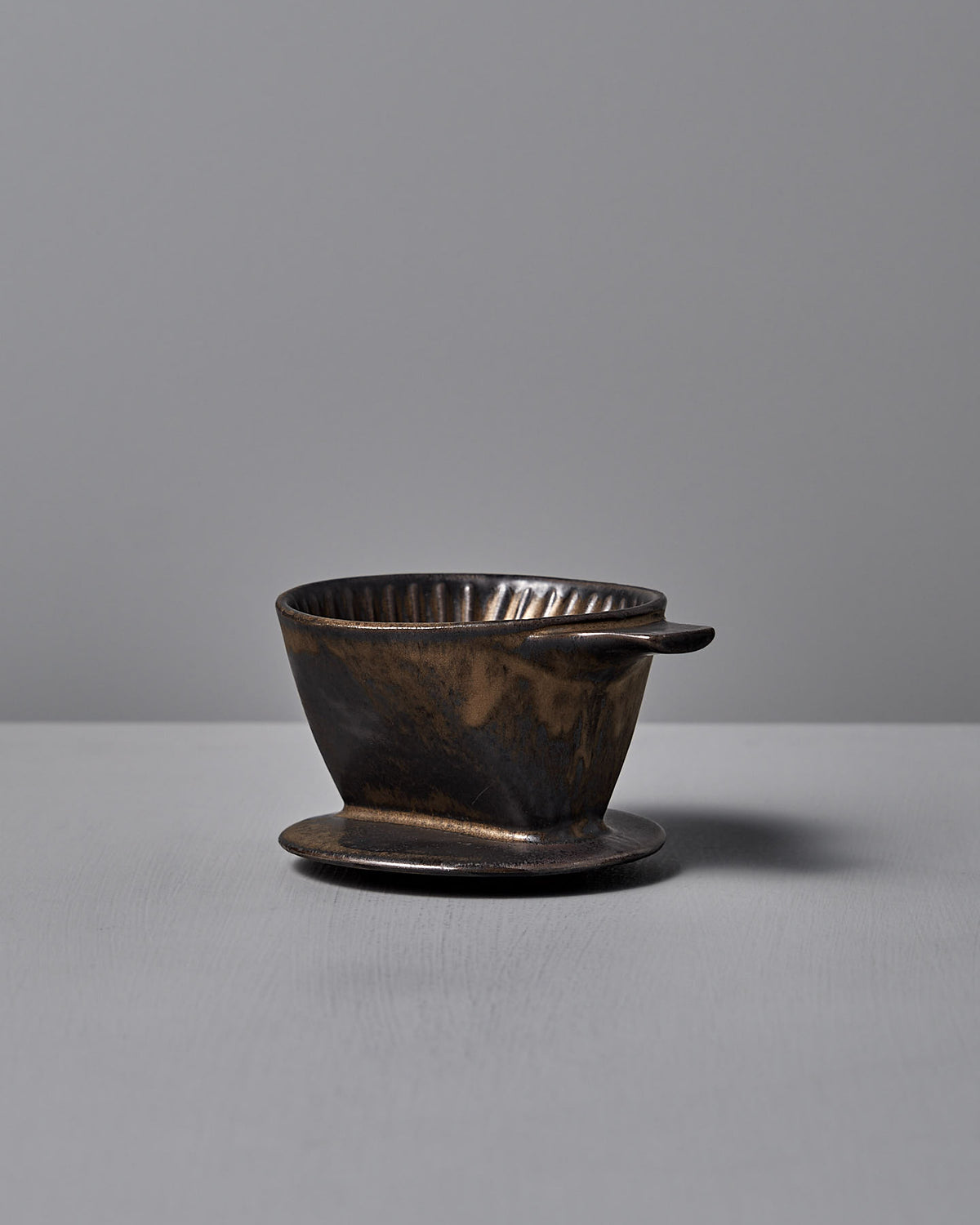 The CHIPS Inc. Mino-yaki Coffee Dripper (2 Cup) in brass elegantly sits on a smooth gray surface against a matching backdrop.