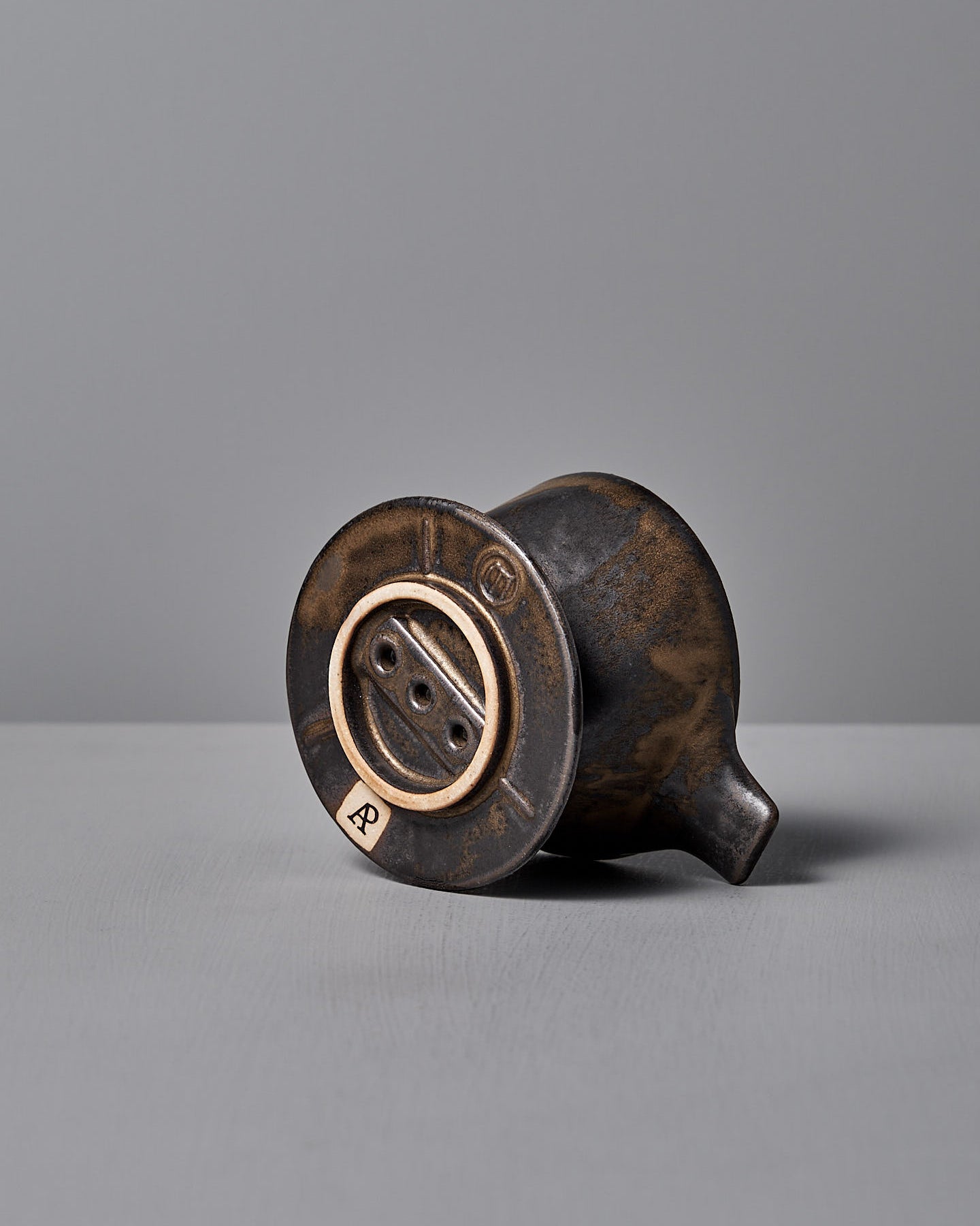 A Mino-yaki Coffee Dripper (2 Cup) – Brass by CHIPS Inc., with a small handle, rests on a matching saucer against a plain gray background.